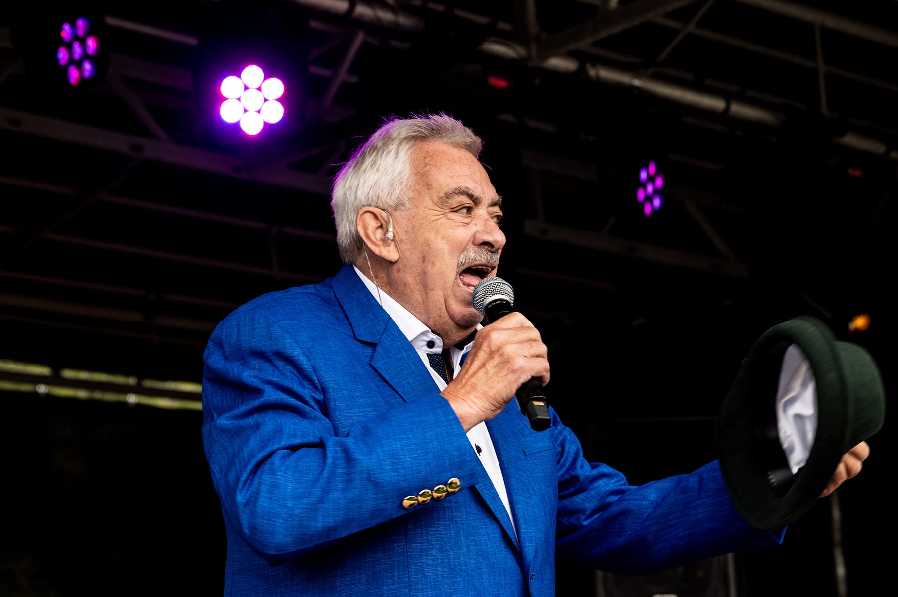 Johnny Reimar synger i mikrofon iført blå jakke med en hat i hånden