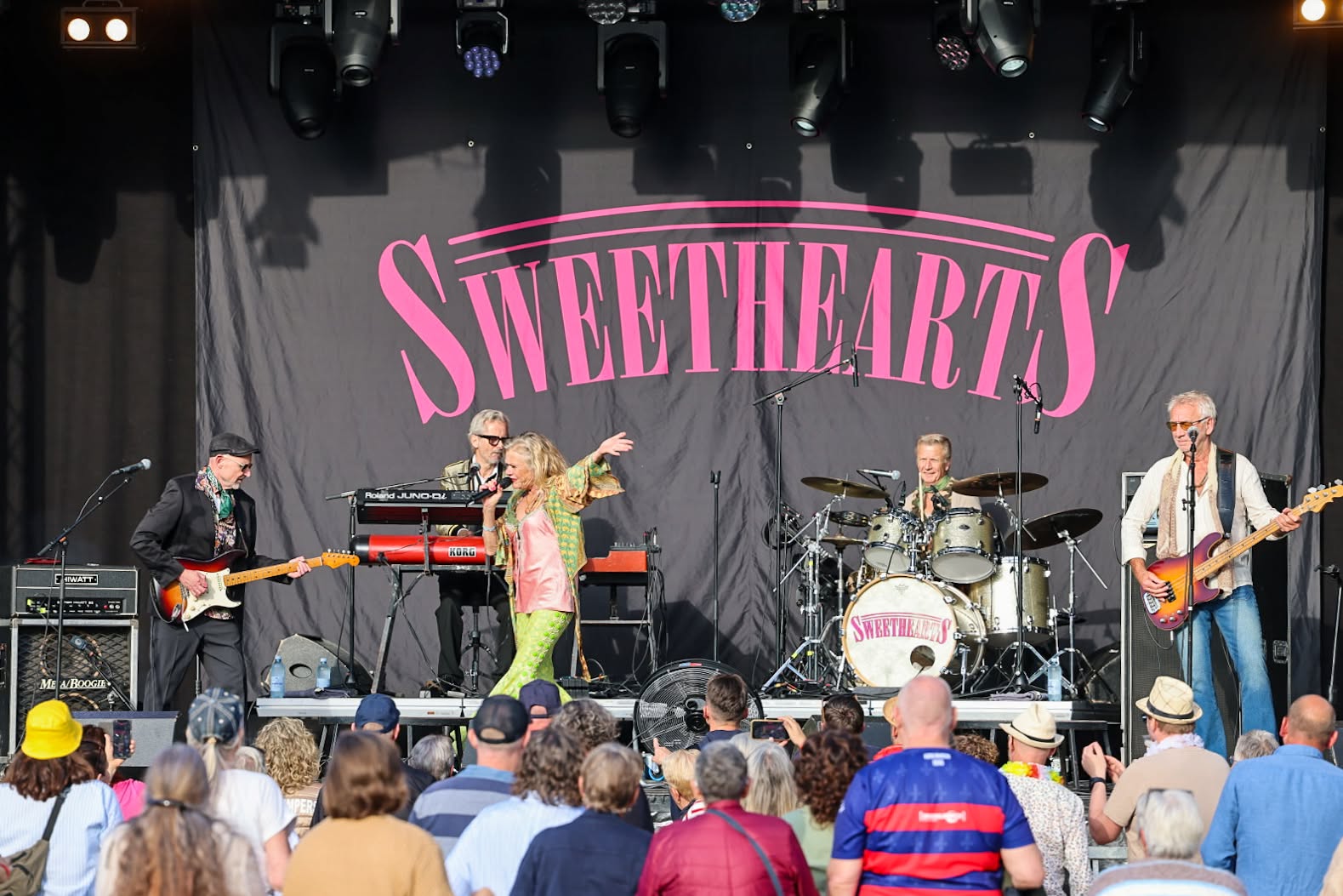 Sweethearts samlet på scenen under orkestrets store lyserøde logo